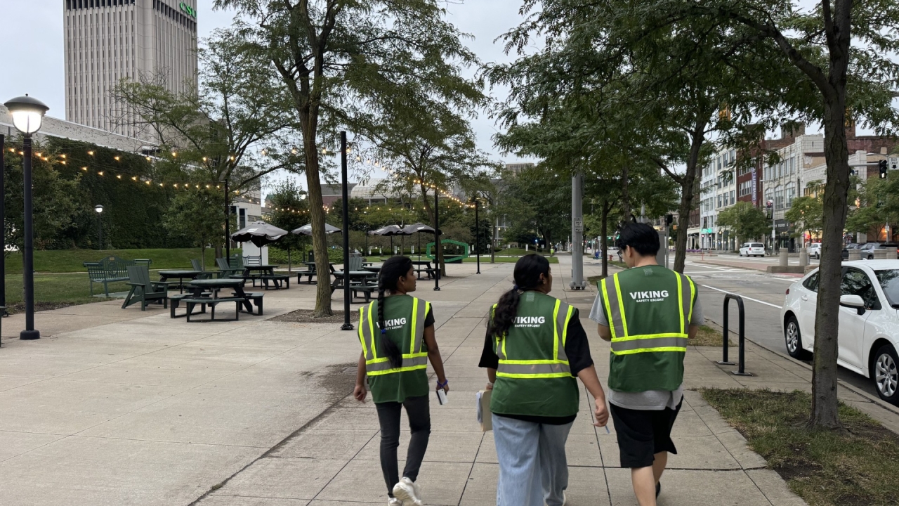 Three students, wearing Green Viking Safety Ambassador vests are walking towards the Student Center near Longship Food Truck